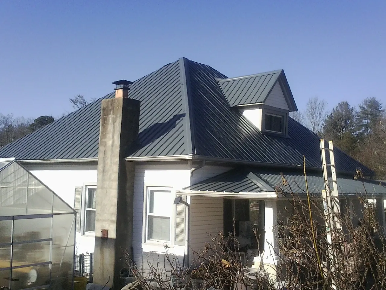 Dark blue standing seam metal roof on a white farmhouse with dormer — Slate & Tile Roof Repair by Roofing Brothers in Persia
