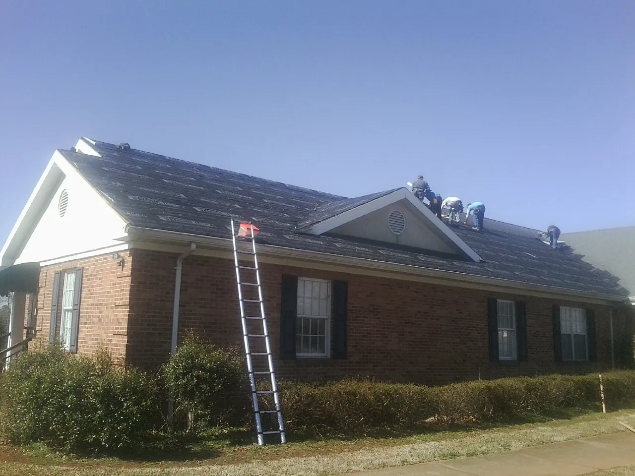 Crew tearing shingles off a brick ranch roof with a ladder set — Emergency Roof Repair work by our crew in Persia