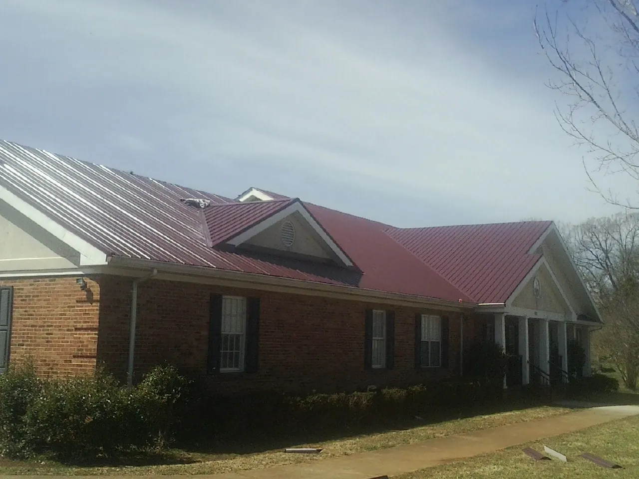 Red metal roof with gabled entries on a long brick building, from a Hail Damage Roof Repair job in Persia