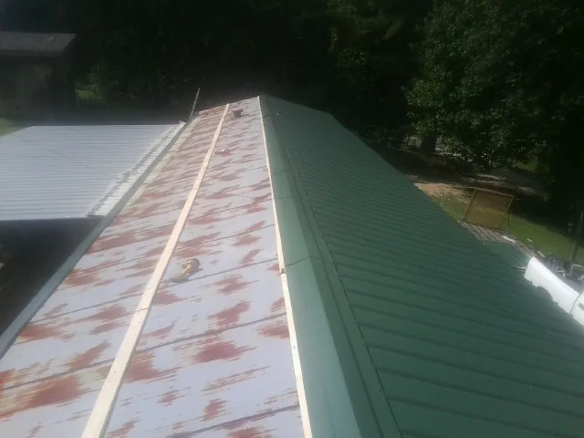 Old rusted panels beside newly installed green metal roofing — Wind Damage Roof Repair by Roofing Brothers in Persia