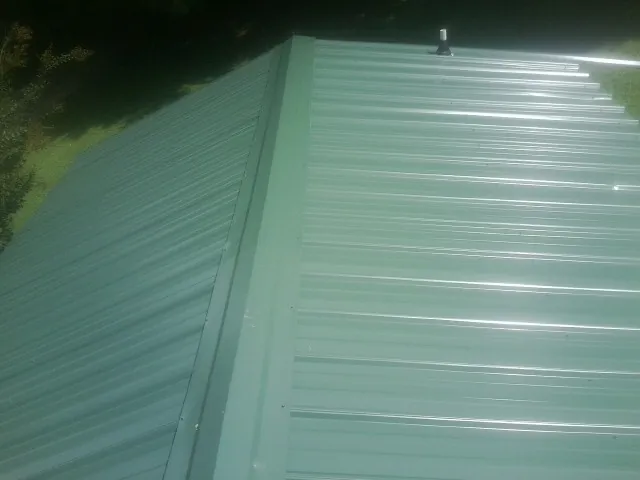 New green metal panels meeting at the ridge of a roof — Flat Roof Repair work by our crew in Persia