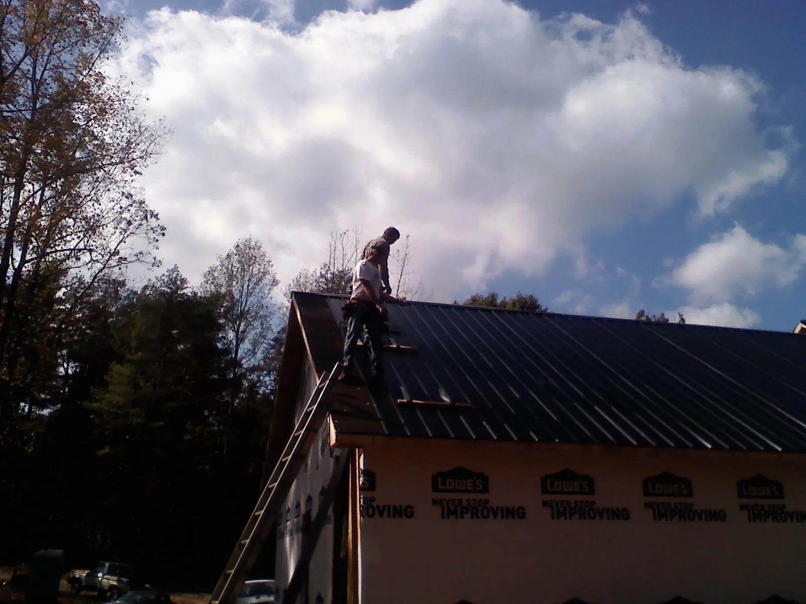 Roofer fastening dark metal panels high against a cloudy sky, from a Roof Inspection job in Persia