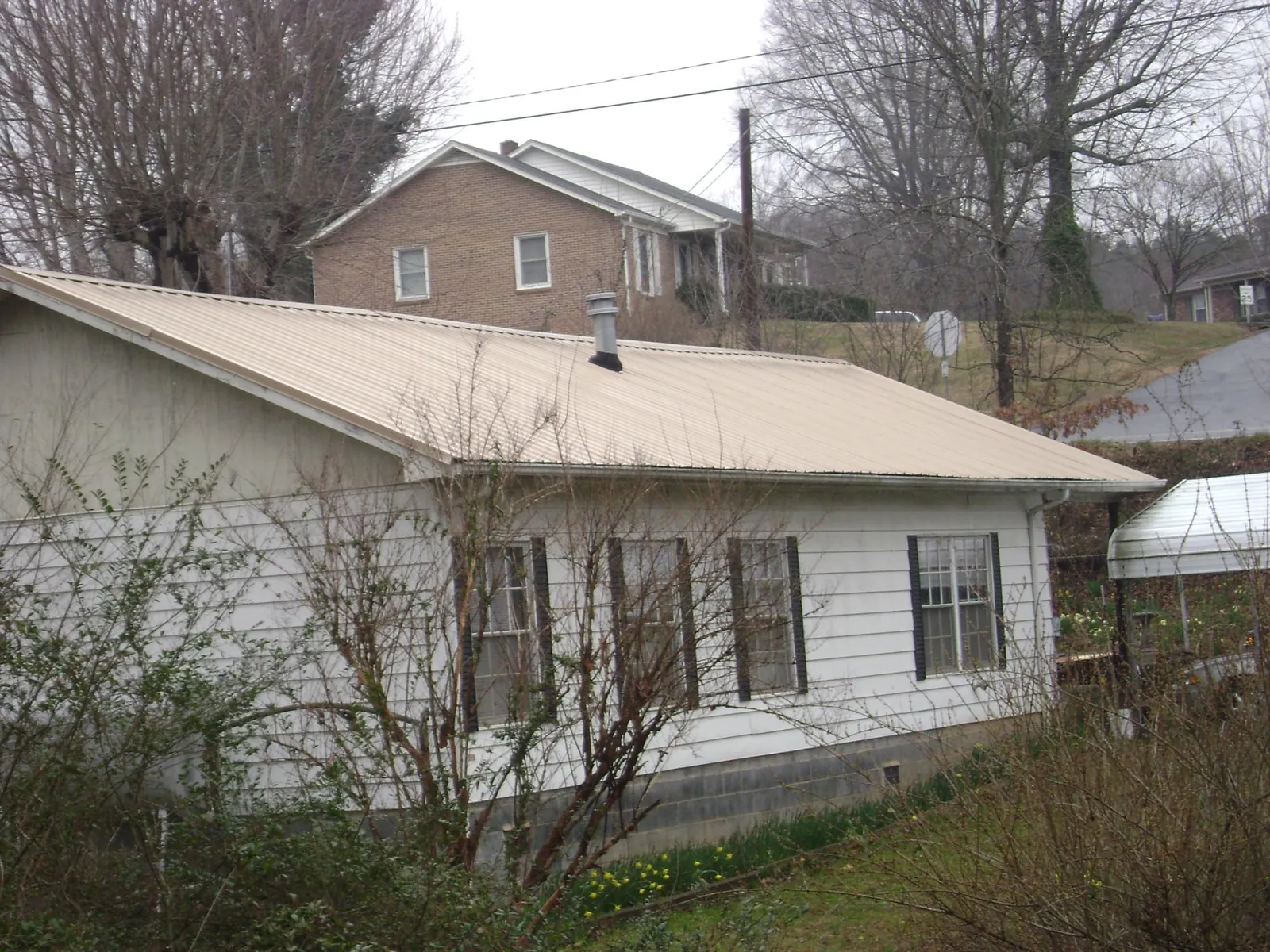 Tan metal roof on a white sided house set into a hillside — Commercial Roofing by Roofing Brothers in Persia
