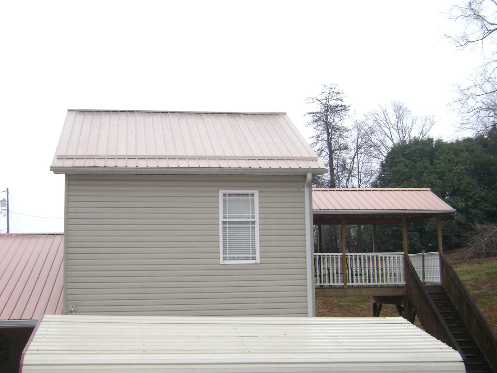 Tan metal roofs on a two story addition and attached porch, from a Roof Replacement job in Persia